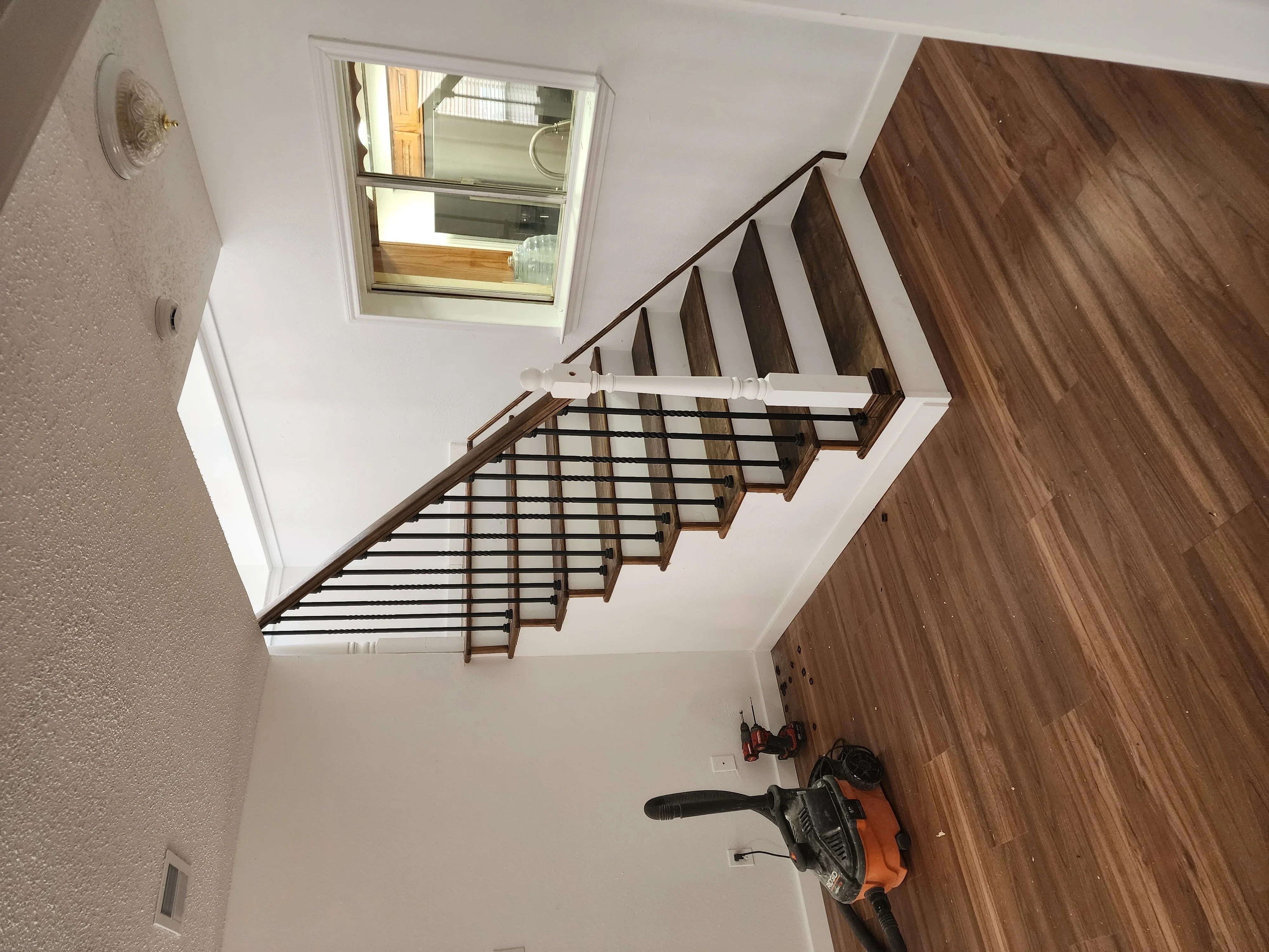 Dark wood staircase with white risers and metal grid railing system under skylight