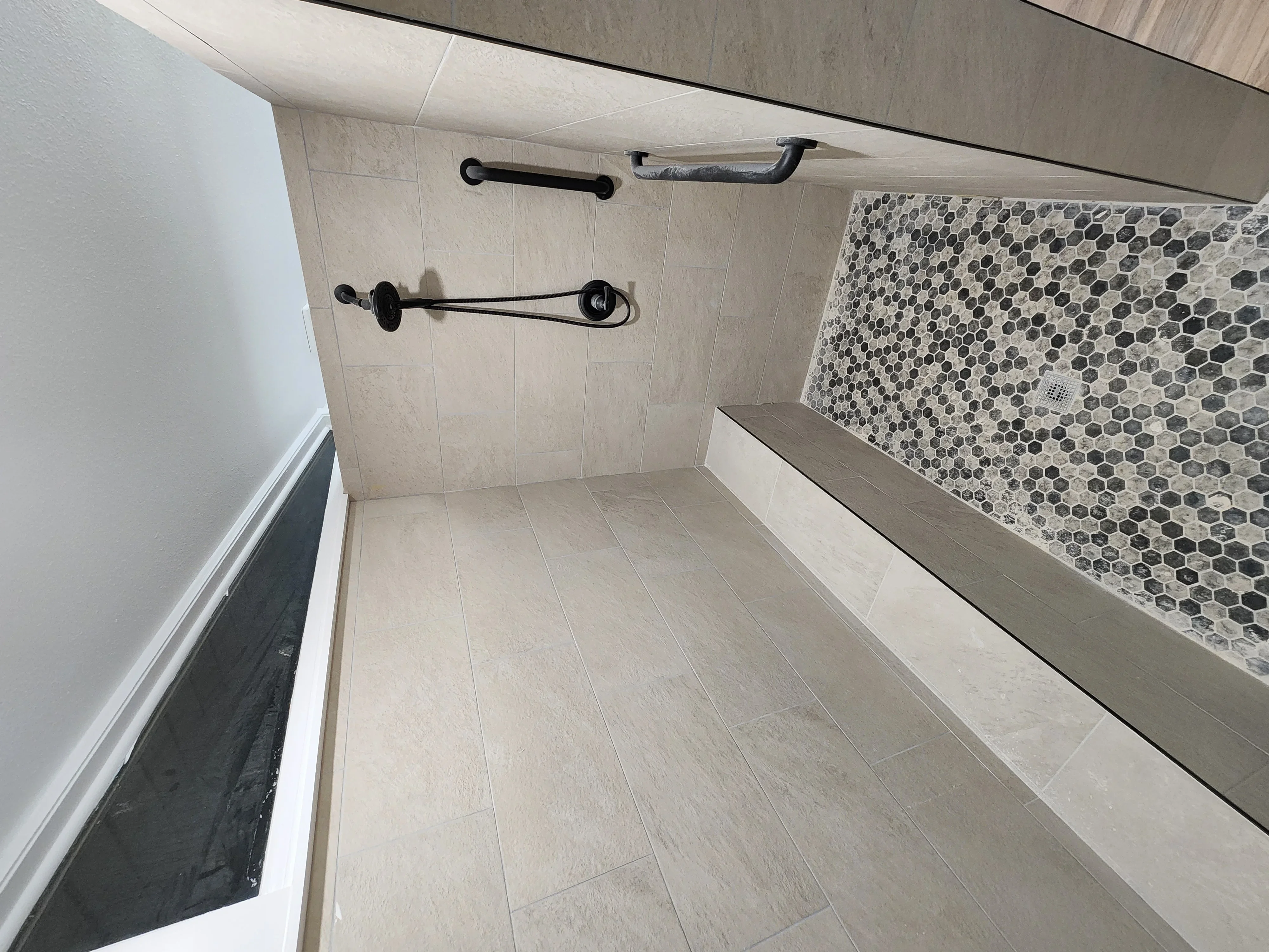 Bathroom with porcelain tile flooring, hexagonal mosaic shower surround, and black metal fixtures