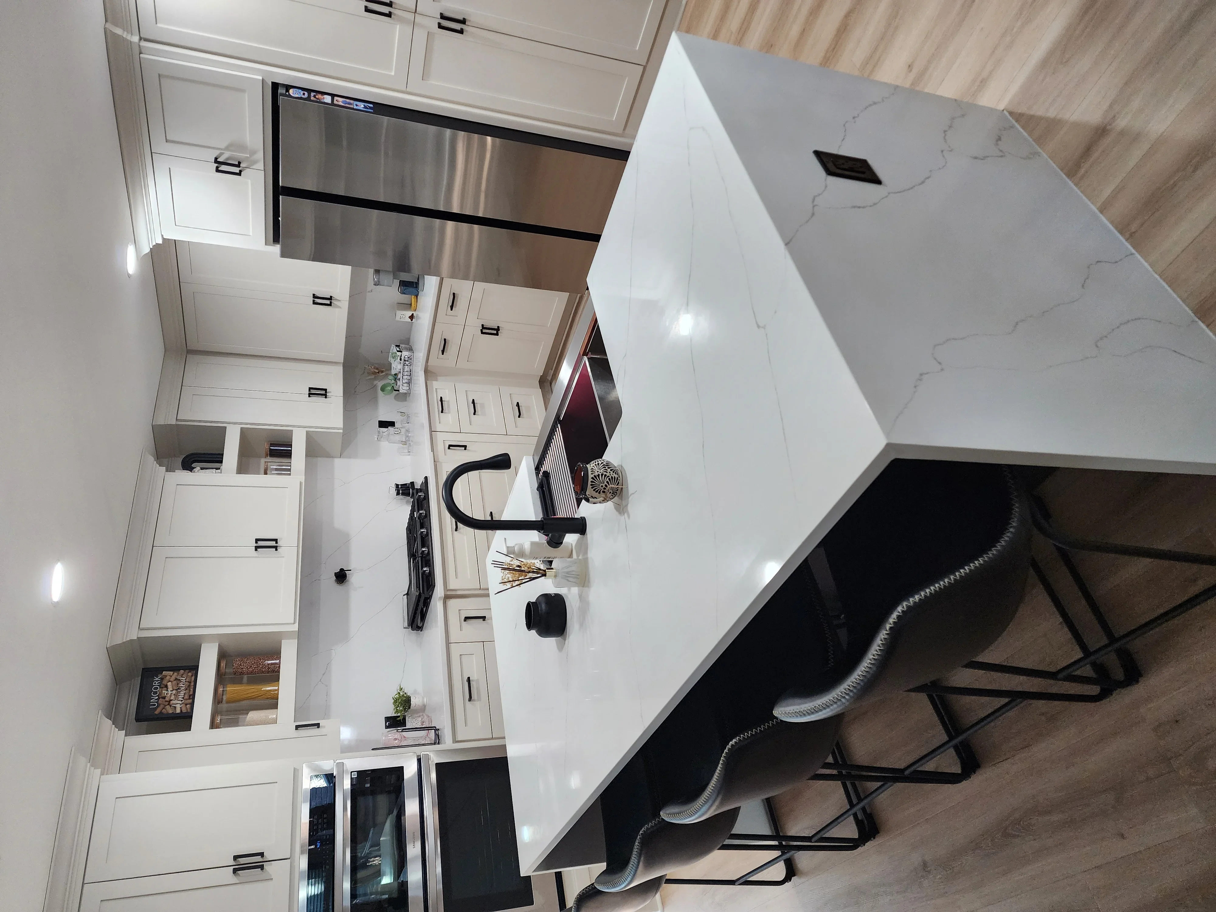 White kitchen cabinets, quartz island countertop, stainless steel appliances, wood flooring